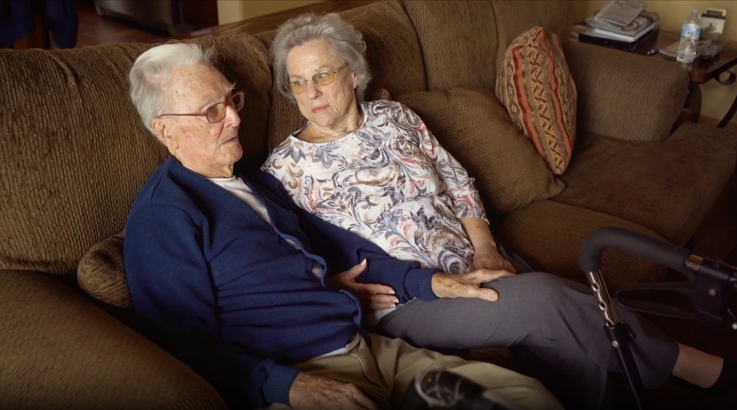 An elderly couple, close together on their couch